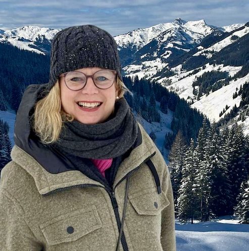 Karina steht entspannt auf einem Berggipfel und sieht glücklich aus, Thema Innehalten lernen.